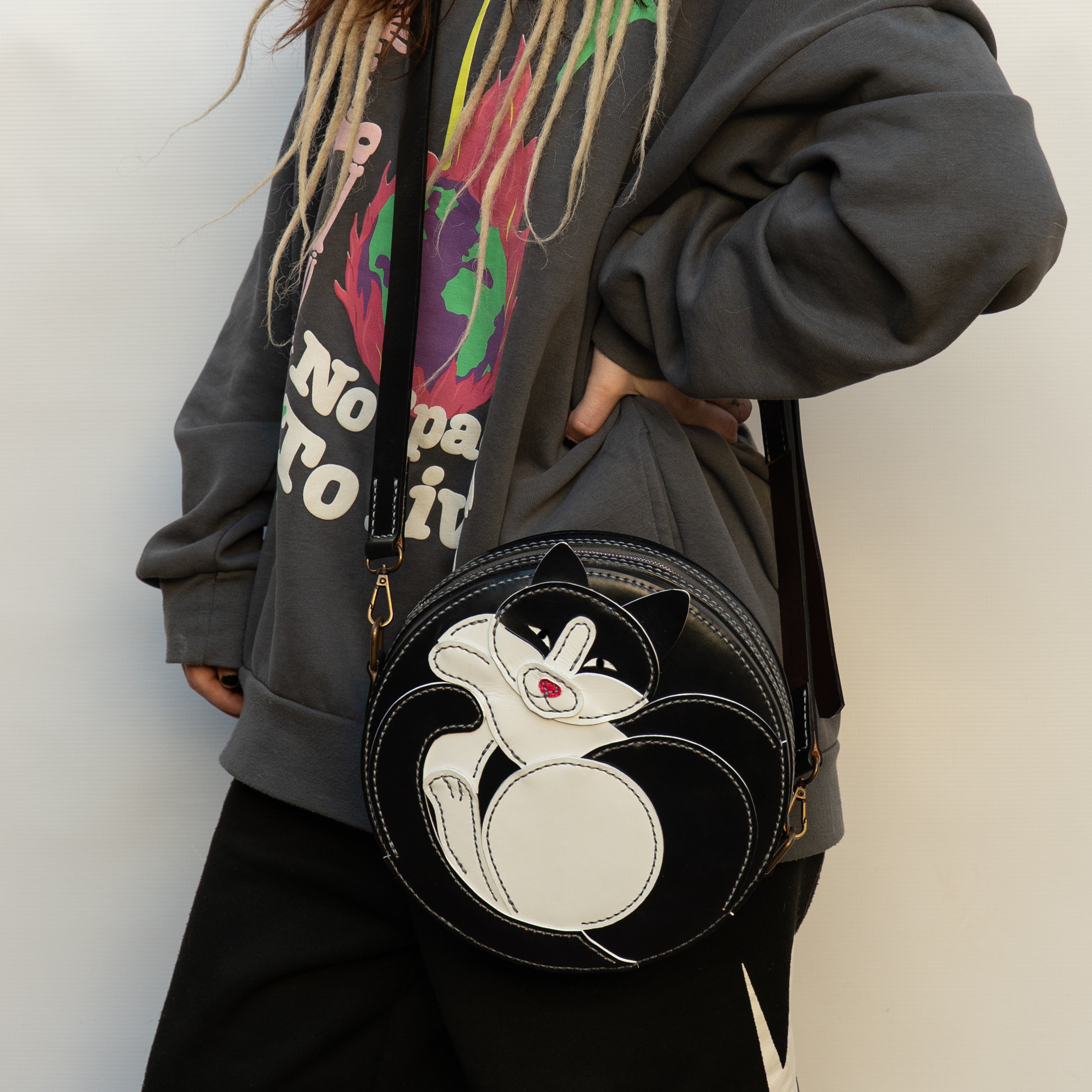Person wearing a dark hoodie with colorful graphics, holding a black crossbody bag with a cat design.