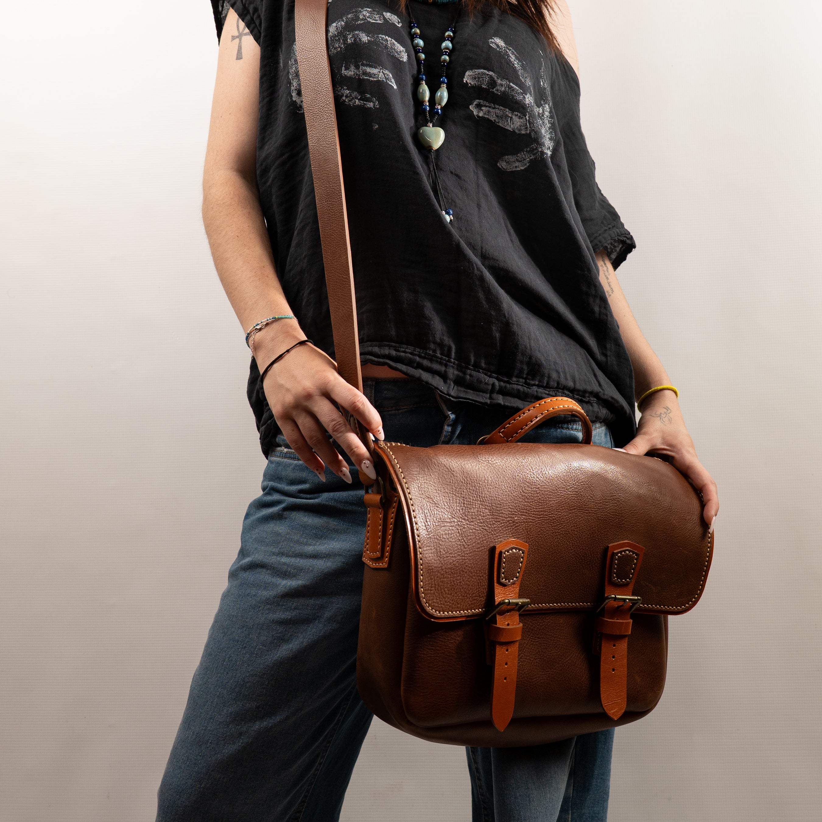 Handmade Morgan Messenger Bag in brown leather with adjustable strap, shown carried by a woman against a white background. Leathercraft design by Vasile and Pavel.