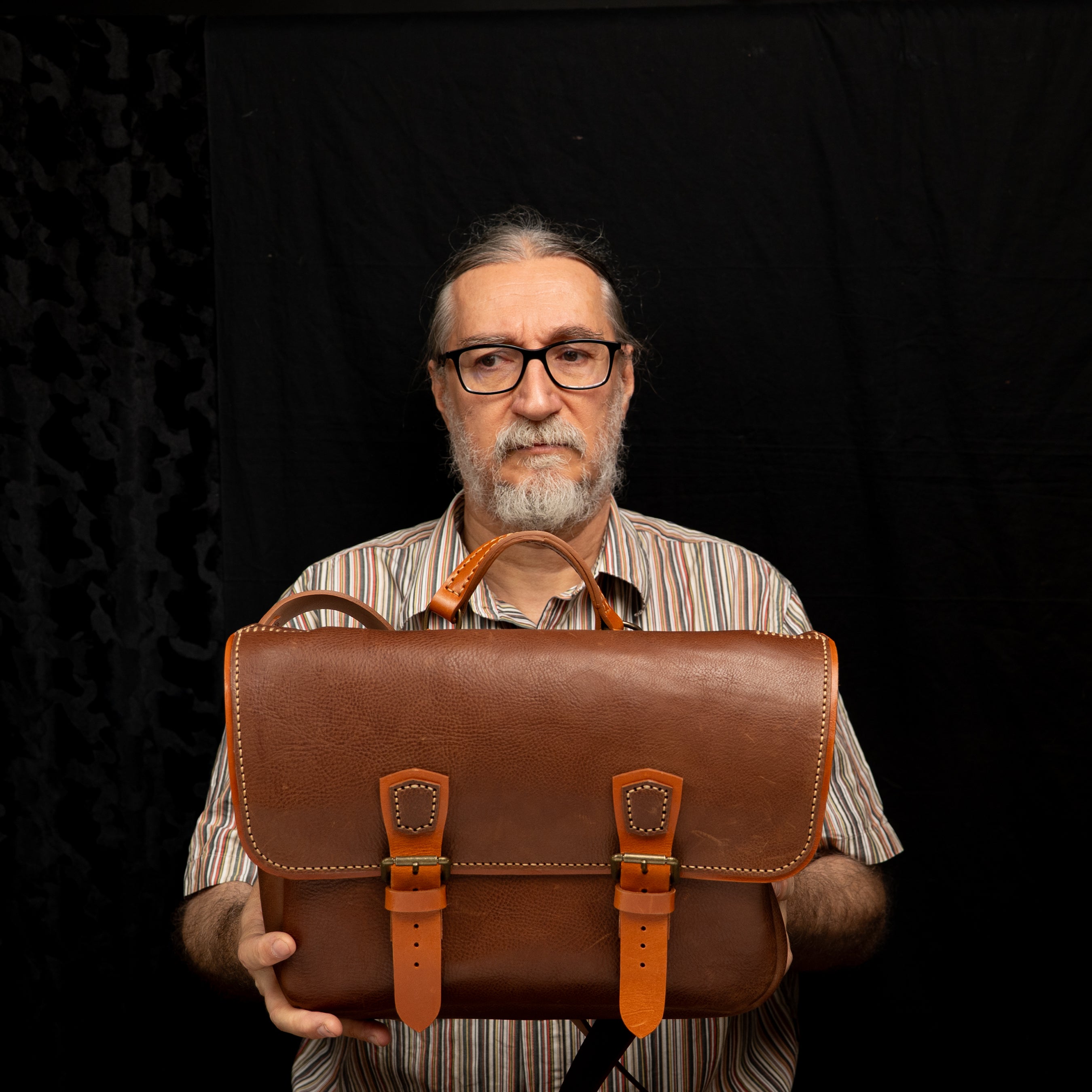 Handmade Morgan Messenger Bag in brown leather with adjustable strap, shown carried by a man against a dark background. Leathercraft design by Vasile and Pavel.