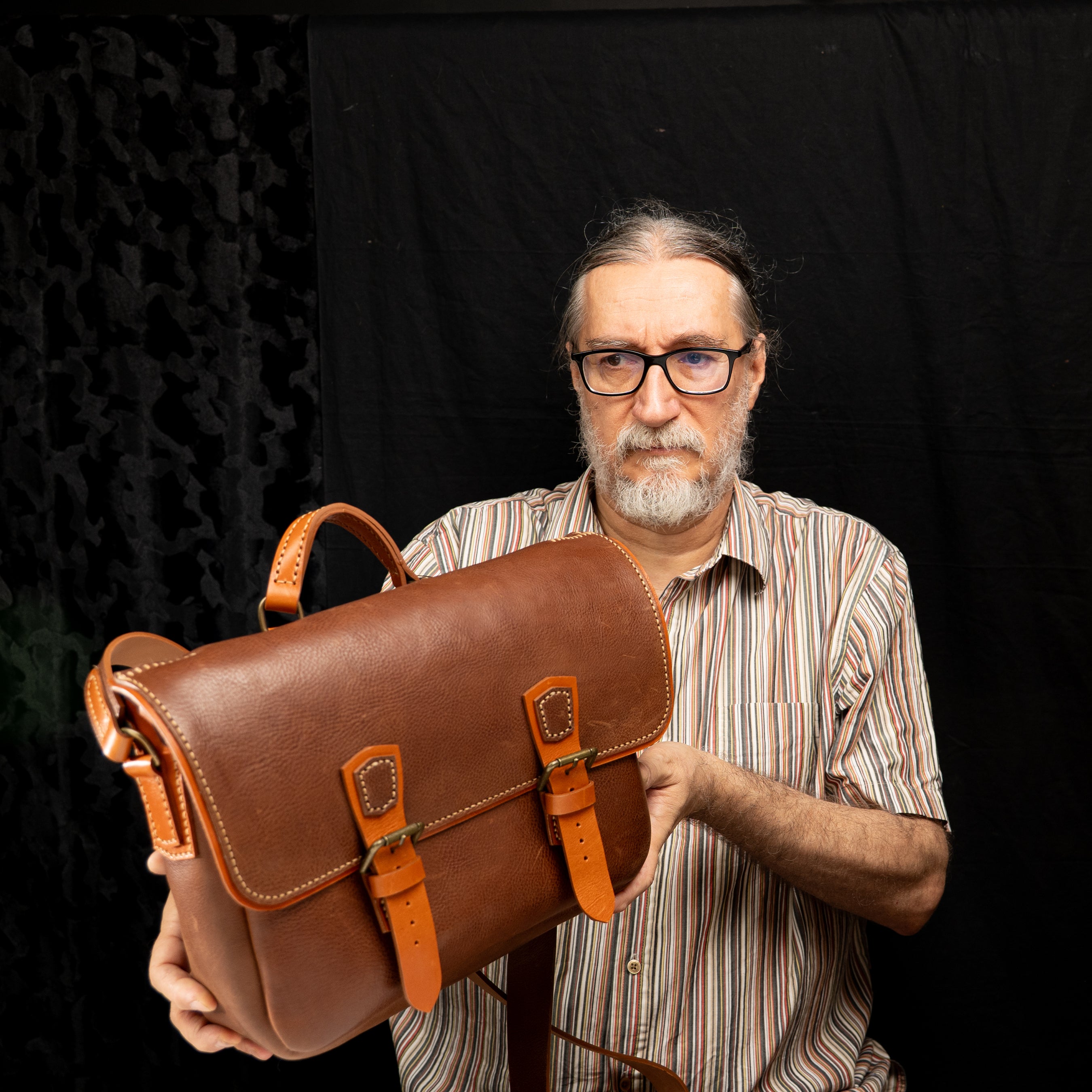 Handmade Morgan Messenger Bag in brown leather with adjustable strap, shown carried by a man against a dark background. Leathercraft design by Vasile and Pavel.