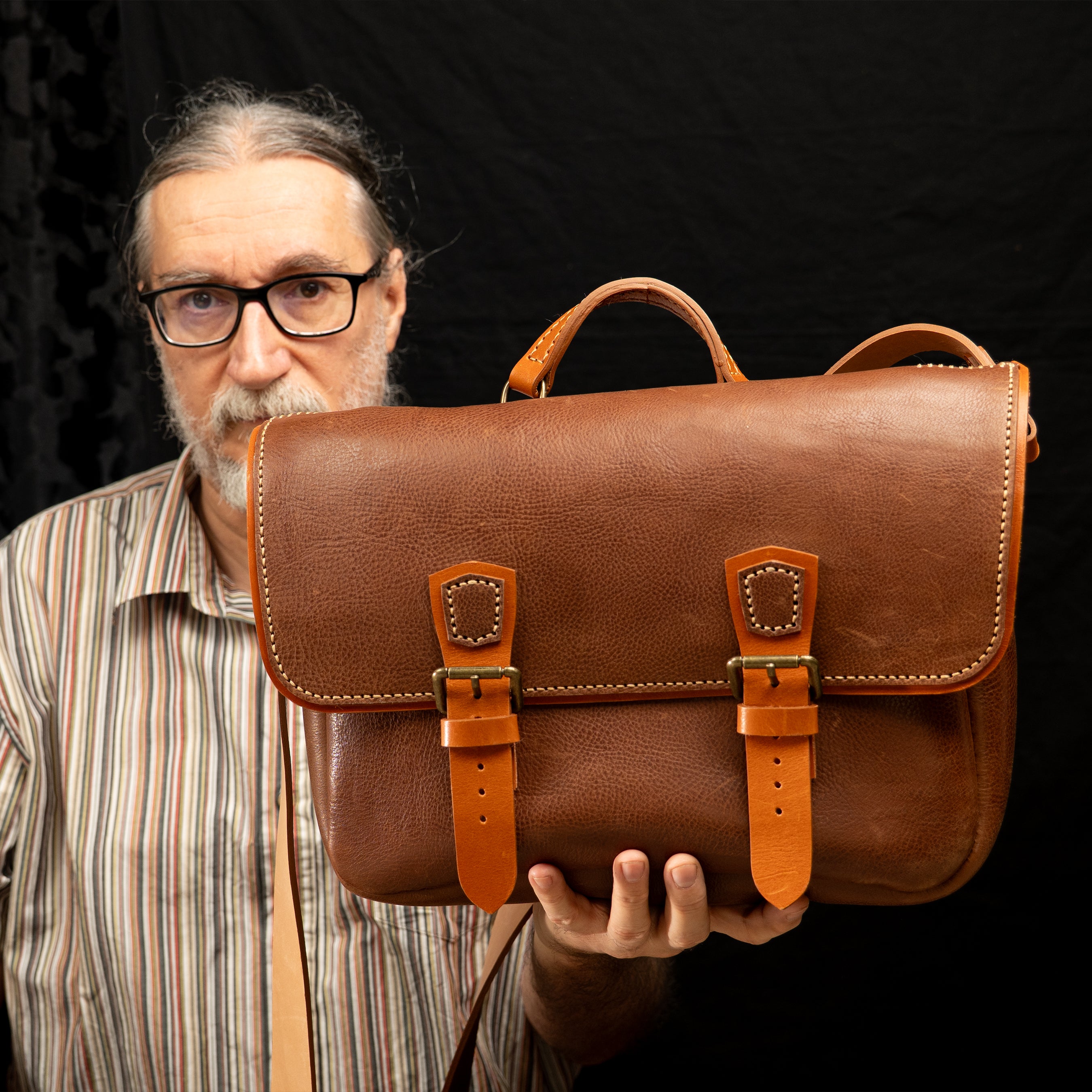 Handmade Morgan Messenger Bag in brown leather with adjustable strap, shown carried by a man against a dark background. Leathercraft design by Vasile and Pavel.